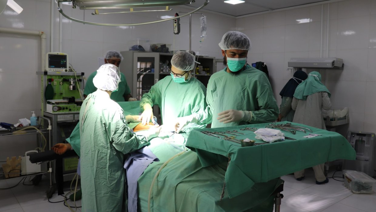 En patient ligger på bordet i en operationssal omgiven av medicinsk personal i gröna kirurgkläder