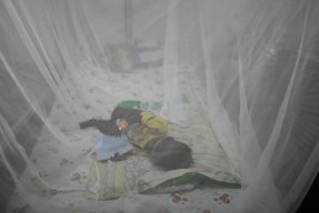 Ett barn ligger under ett myggnät på en säng i Sydsudan.