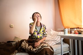 en kvinna sitter på en sjukhussäng och håller för ena ögat för ett syntest