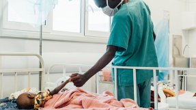 Tvååriga Sheku Kamara, som ligger på sängen på Läkare Utan Gränsers sjukhus i Kenema, Sierra Leone, håller en anställd i handen.