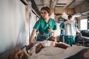En patient med bandage på armen ligger på en bår och blir omhändertagen av en sjuksköterska